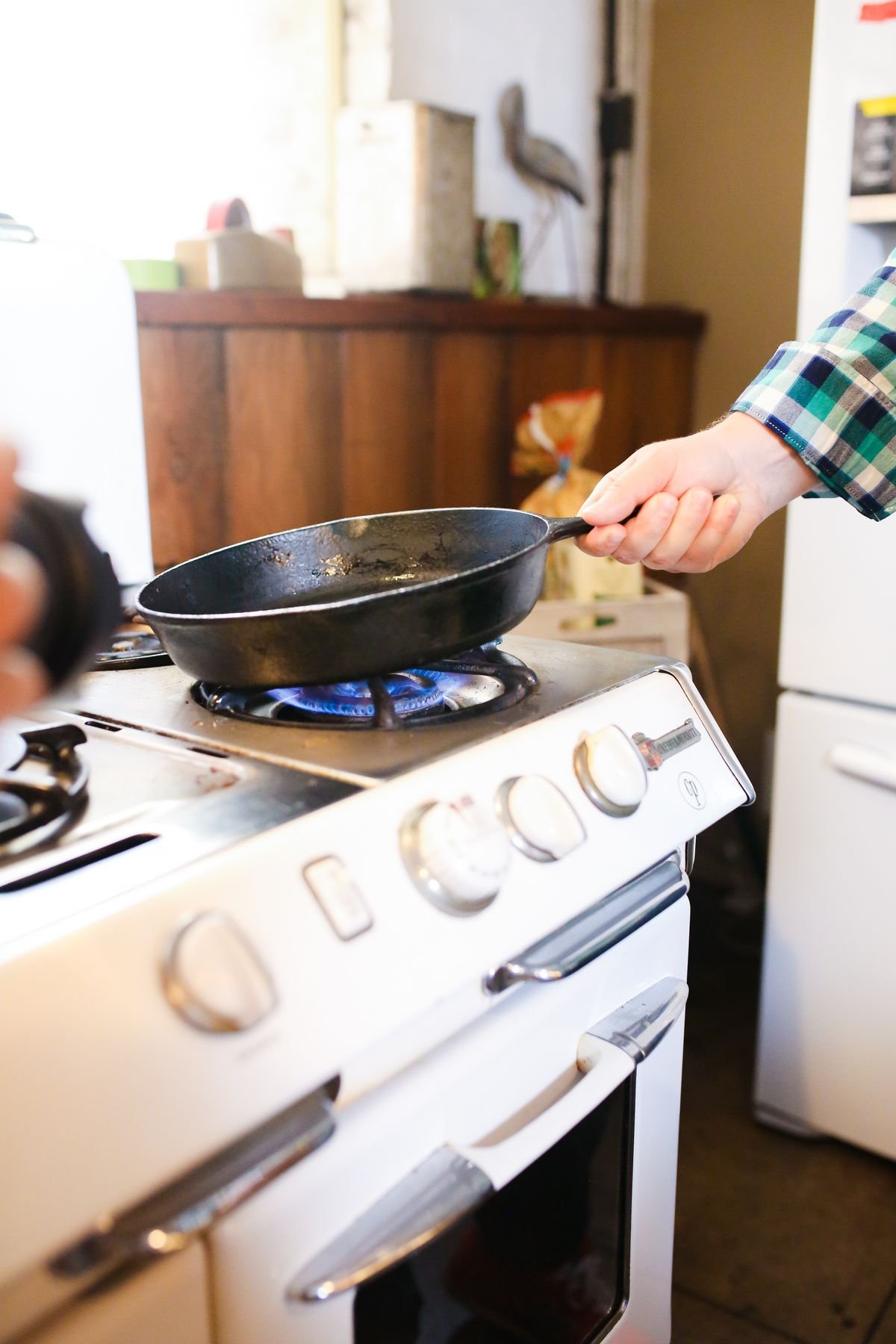 Hand holding a black skillet over the blue flame of a gas stove burner