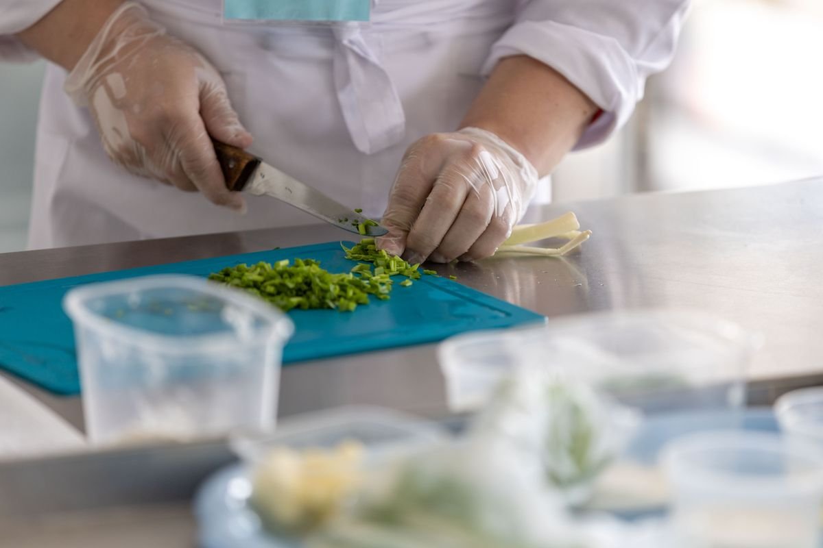 Gloved hands finely chopping fresh green herbs on a cutting board